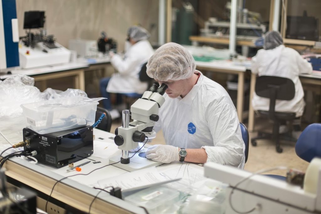 Medical device manufacturing technician examining device under microscope